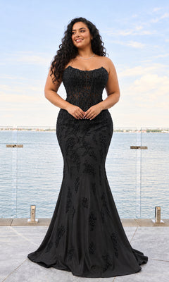 A woman in a black, strapless, bead-embroidered Long Plus-Size Prom Dress: Faviana 11600E stands on a balcony overlooking the water.