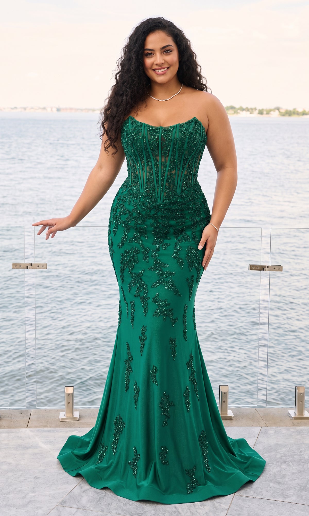 A plus-size woman wears the Faviana 11600E, a dark emerald, strapless corset gown with a floor-length silhouette and beaded floral embroidery.