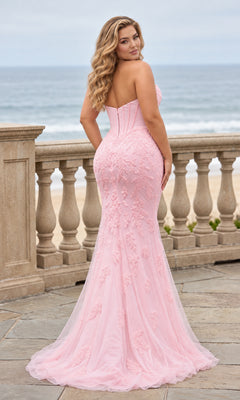 A woman in a light pink, floor-length mermaid Long Plus-Size Prom Dress: Faviana 11604E with floral lace appliqué, standing on a stone patio overlooking the ocean.