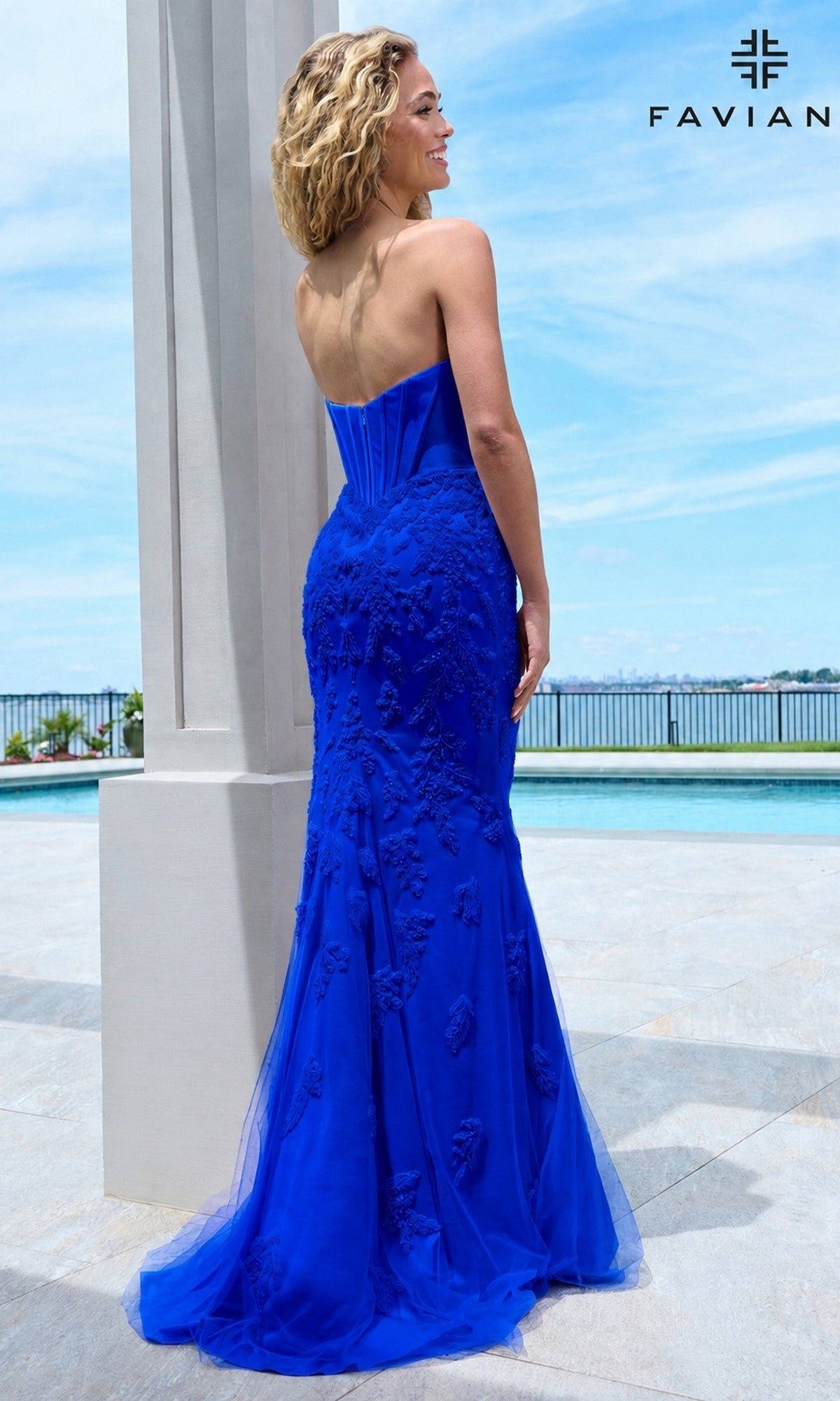 A person wearing a royal blue Faviana 11604 strapless corset prom dress with an embroidered skirt, standing on a patio by a pool.