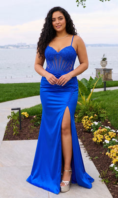 A person wears a royal blue, floor-length Faviana 11605E plus-size prom dress with a corset bodice featuring lace appliques and a high thigh slit.