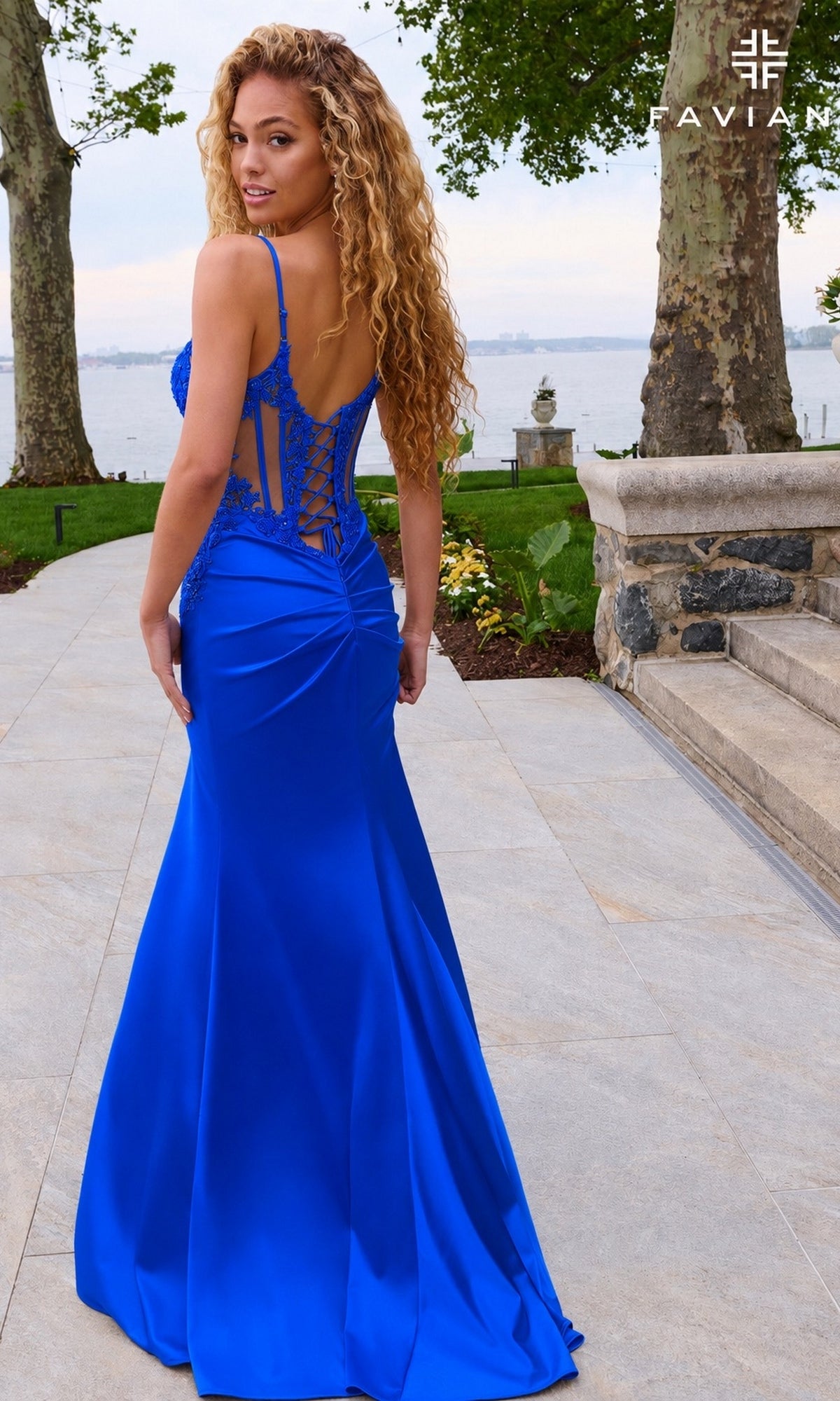 A woman wearing a royal blue, floor-length satin Faviana 11605 prom dress with spaghetti straps and a lace-up corset bodice.
