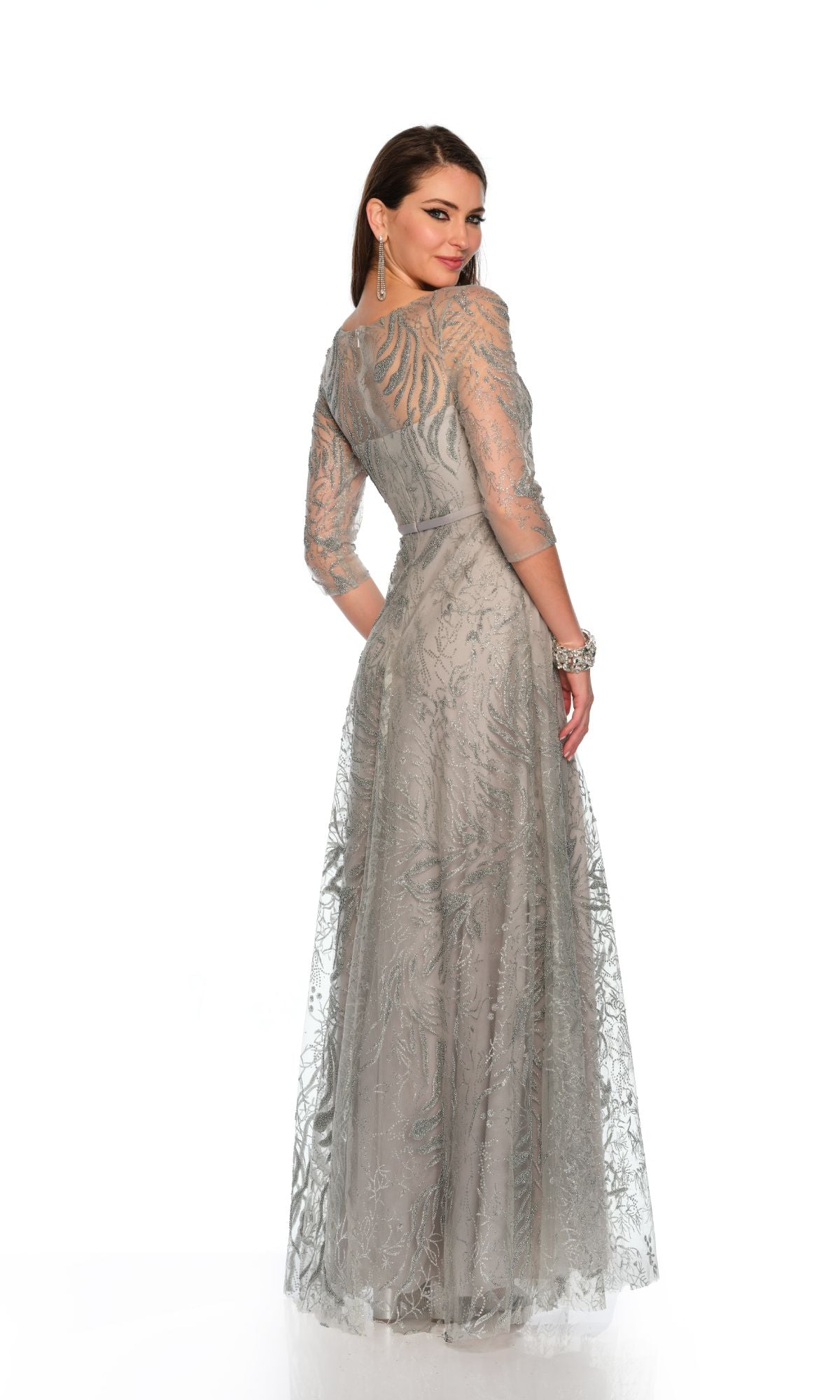 A woman poses with her back turned and head over her shoulder against a white background, wearing the Long Formal Dress 11606 by Dave and Johnny—a light gray a-line gown with sheer sleeves and a sweetheart neckline.