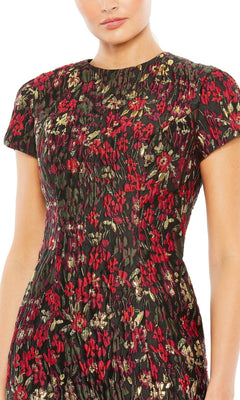 Woman wearing the Mac Duggal 11613 Short Floral Wedding Guest Dress, a fitted short-sleeved brocade party dress with red and gold floral patterns on a dark background. Upper body visible; face partially out of frame.