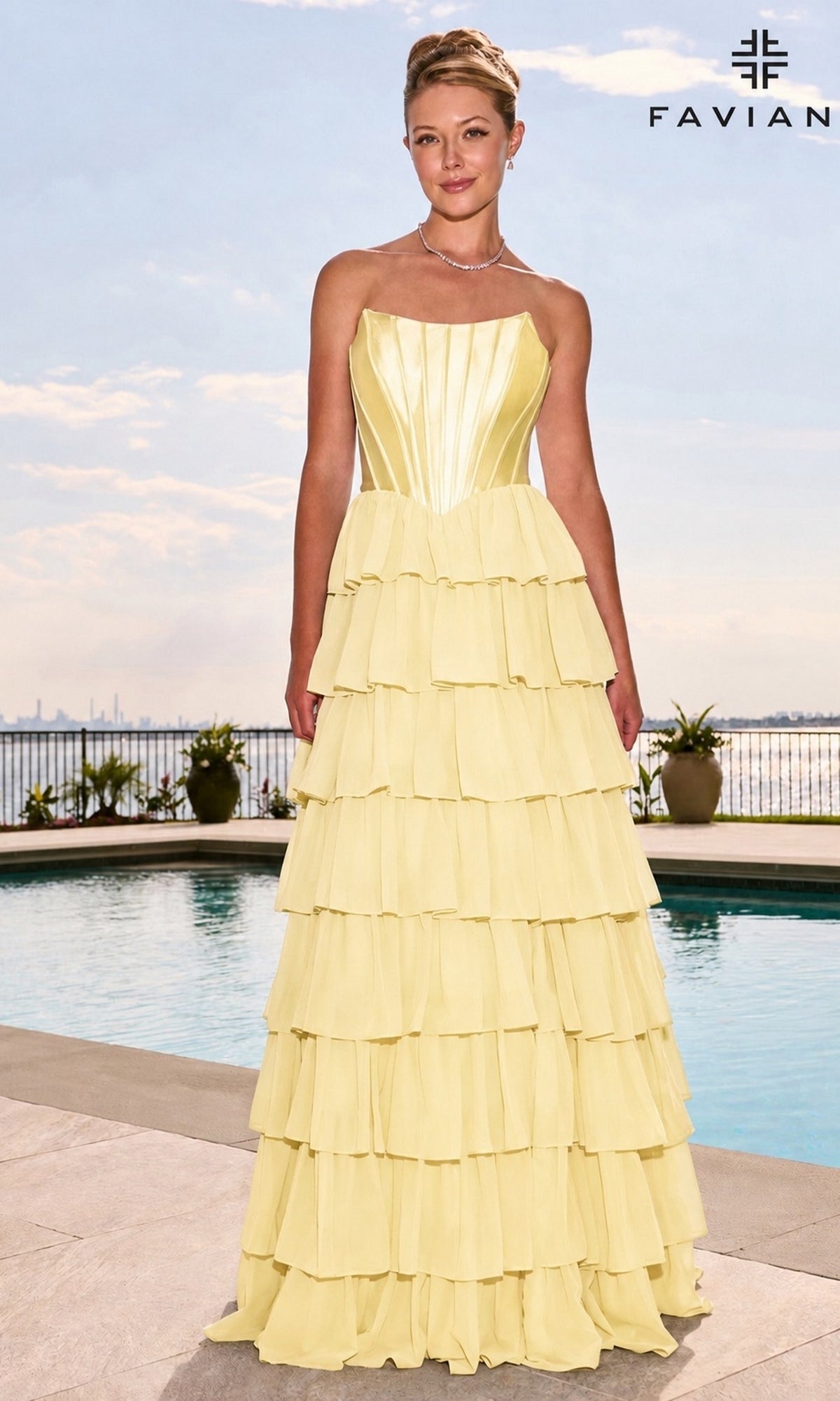 A woman wearing a light yellow Faviana 11631 long prom dress with a strapless, structured satin corset bodice and a multi-tiered ruffled skirt stands by a swimming pool.