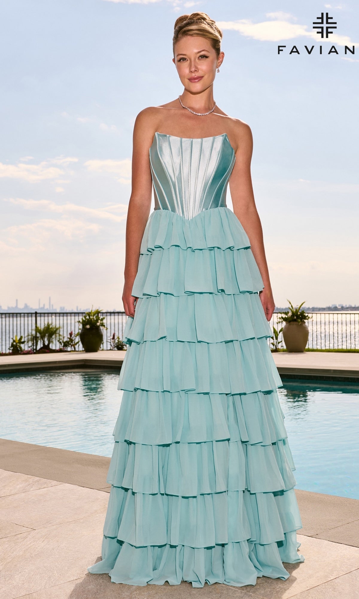 A woman wearing a light blue Faviana 11631 strapless tiered floor-length gown with a satin corset bodice standing by a swimming pool.
