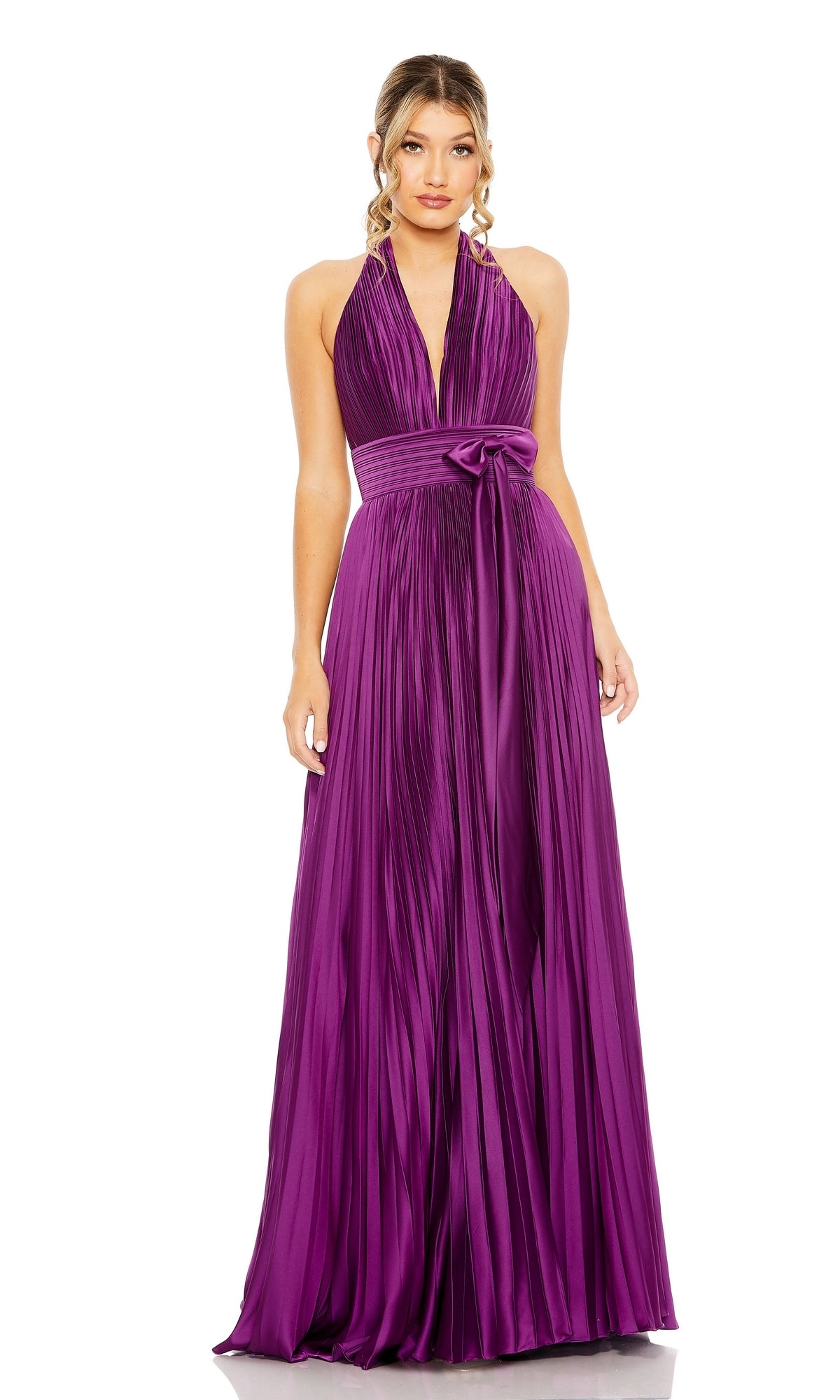 A woman wearing the Long Formal Dress 11636 by Mac Duggal—a sleeveless, floor-length deep purple halter dress with a pleated skirt and tied waistband—stands against a white background.