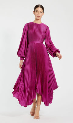 A woman models the Mac Duggal 11638 Fuchsia Midi Wedding Guest Dress, showcasing elegant pleats, long sleeves, a fitted waist, and flowy skirt. She pairs it with strappy heels and poses against a plain background.