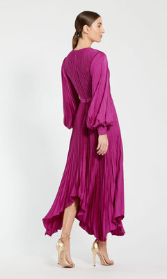 A woman faces away in the Mac Duggal 11638 Fuchsia Midi Wedding Guest Dress with pleats and long sleeves, paired with gold high-heeled sandals, set against a plain light background.