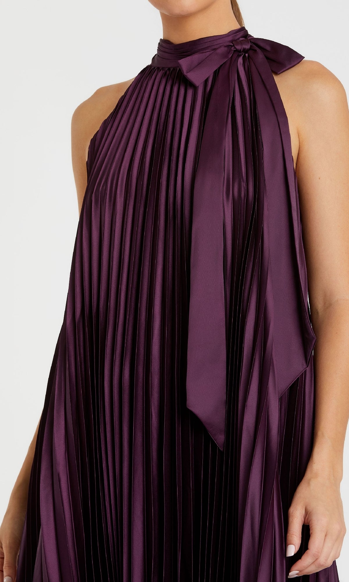 Person wears the Mac Duggal 11639, a long plum purple formal dress featuring a sleeveless, pleated satin design with high neck and tied bow details.