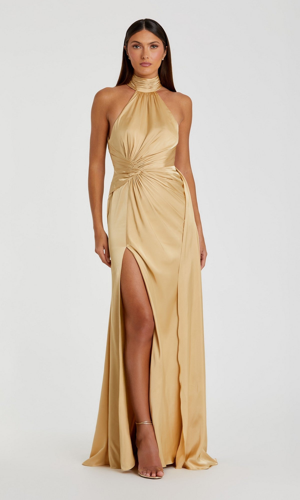 A woman models the Mac Duggal 11642 high-neck long prom dress in gold, featuring a halter neckline, high slit, and gathered waist, standing against a plain white background.