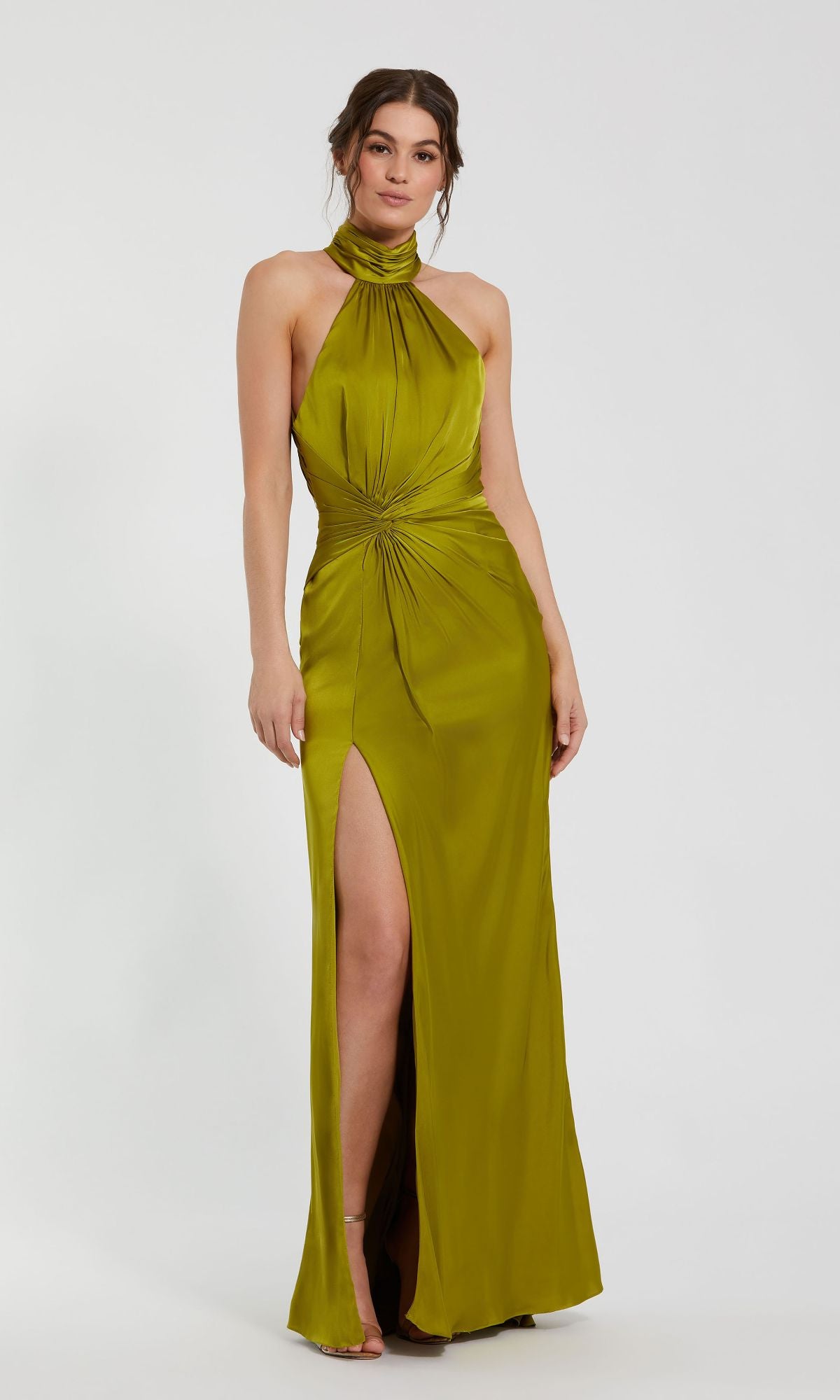 A woman wears the Mac Duggal 11642 High-Neck Long Prom Dress, an olive green sleeveless gown featuring a halter neck, front knot detail, and high slit, set against a plain light background.