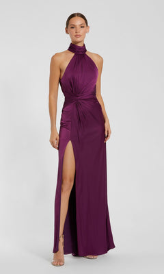 A woman in the Mac Duggal 11642 high-neck long prom dress, sleeveless and floor-length in purple with a gathered waist and thigh-high slit, paired with strappy heels.