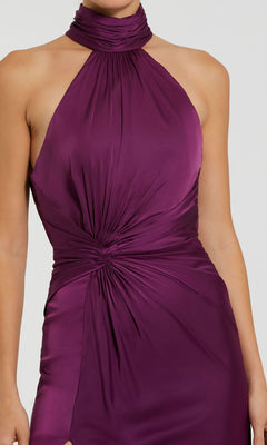 A person wearing the Mac Duggal 11642 High-Neck Long Prom Dress, a sleeveless satin evening gown in deep purple with a halter neckline and ruched waist detailing.