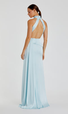 A woman models the Mac Duggal 11642 High-Neck Long Prom Dress in light blue, featuring a backless halter neckline, as she stands facing slightly away against a plain background.