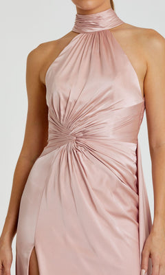 A person wearing the Mac Duggal 11642 High-Neck Long Prom Dress, featuring a sleeveless design, light pink satin fabric, a high neckline, and ruched waist detailing.