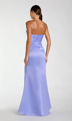 A woman stands facing away, wearing the Sherbet Orange Long Prom Dress by Mac Duggal (style 11653), a strapless, floor-length gown with a fitted bodice and flared skirt, perfect for prom.