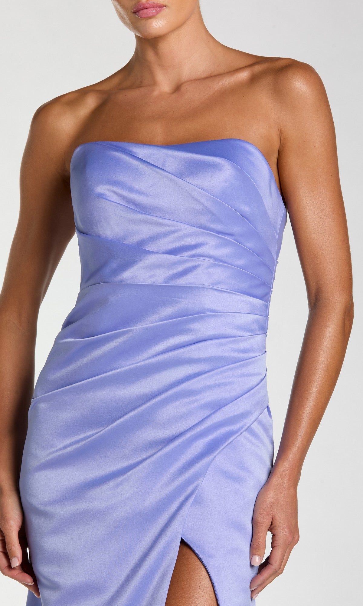 A woman wearing a strapless, fitted Sherbet Orange Mac Duggal 11653 long prom dress with ruched detailing and a thigh-high slit.