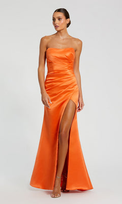 A woman stands against a plain background wearing the Mac Duggal 11653 long prom dress in sherbet, featuring a strapless satin design with a thigh-high slit.