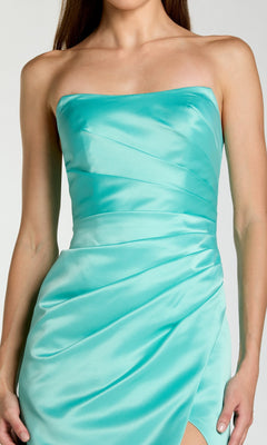 A woman wearing a strapless, fitted, sherbet orange satin formal dress by Mac Duggal (11653), featuring a wrapped, ruched design and a side slit.