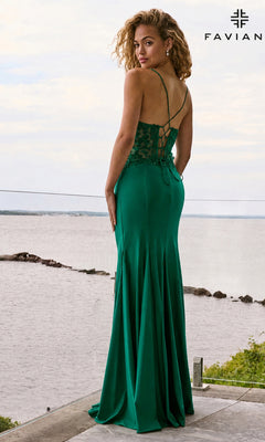 A woman in a dark emerald Faviana 11657 long prom dress with a V-neck, lace bodice, and corset back stands on a balcony overlooking a body of water.