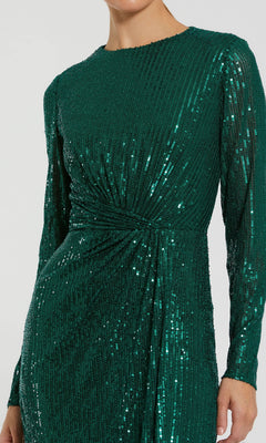 A person wearing the Mac Duggal 11659 long sleeve sequin formal dress in emerald green, featuring a gathered twist detail at the waist.
