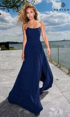 A person in a navy Faviana 11672 strapless corset prom dress with a fitted bodice and front slit walking on a patio overlooking a body of water.