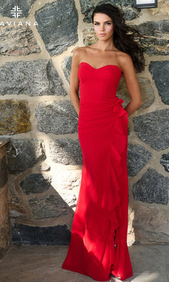 A woman wears a red Faviana 11673 long prom dress, featuring a strapless neckline and a ruffled side detail, while standing against a stone wall.