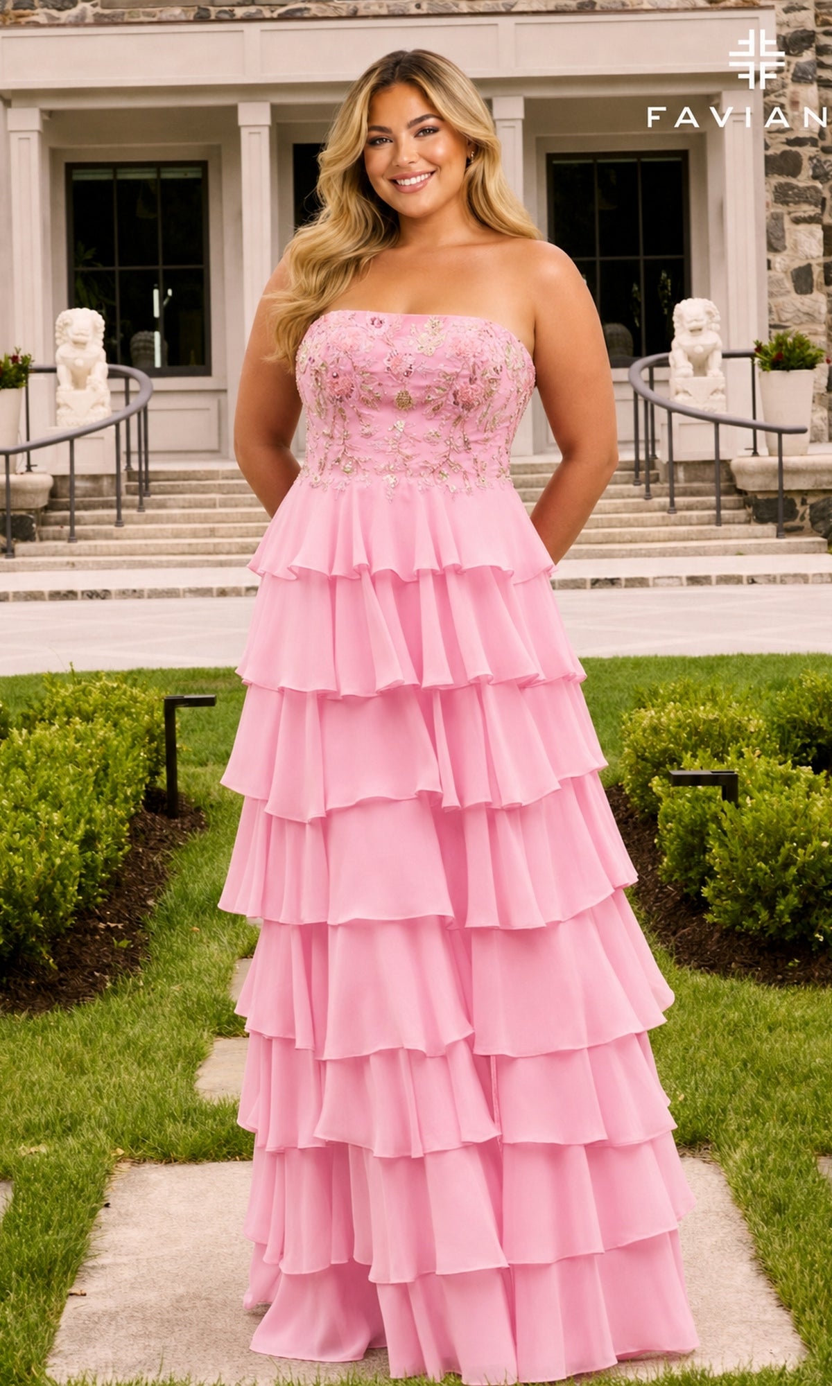 A person wearing the Long Plus-Size Prom Dress: Faviana 11675E, a light pink gown featuring a strapless, floral-appliqued bodice and a tiered, ruffled floor-length skirt.