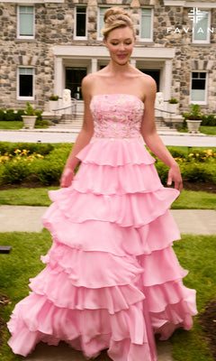 A person wears a Faviana 11675 long prom dress, a strapless pink gown with floral applique, an embroidered bodice, and a tiered skirt, standing on a lawn in front of a stone building.
