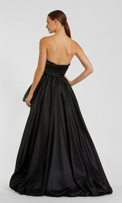 A woman stands facing away from the camera against a plain background, wearing the Mac Duggal 11685 Strapless Balloon Prom Dress featuring a floor-length, full skirt.
