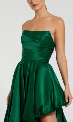 A woman wearing the Strapless Balloon Prom Dress: Mac Duggal 11685, an emerald green satin gown with a fitted bodice and flared, asymmetrical skirt.