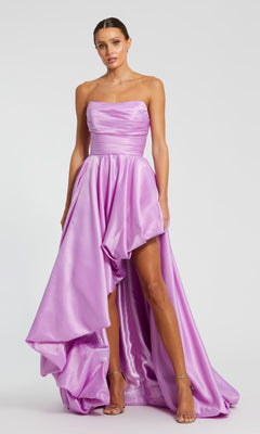 A woman stands against a plain background wearing the Strapless Balloon Prom Dress: Mac Duggal 11685, a lavender satin high-low gown with a fitted bodice and voluminous skirt.