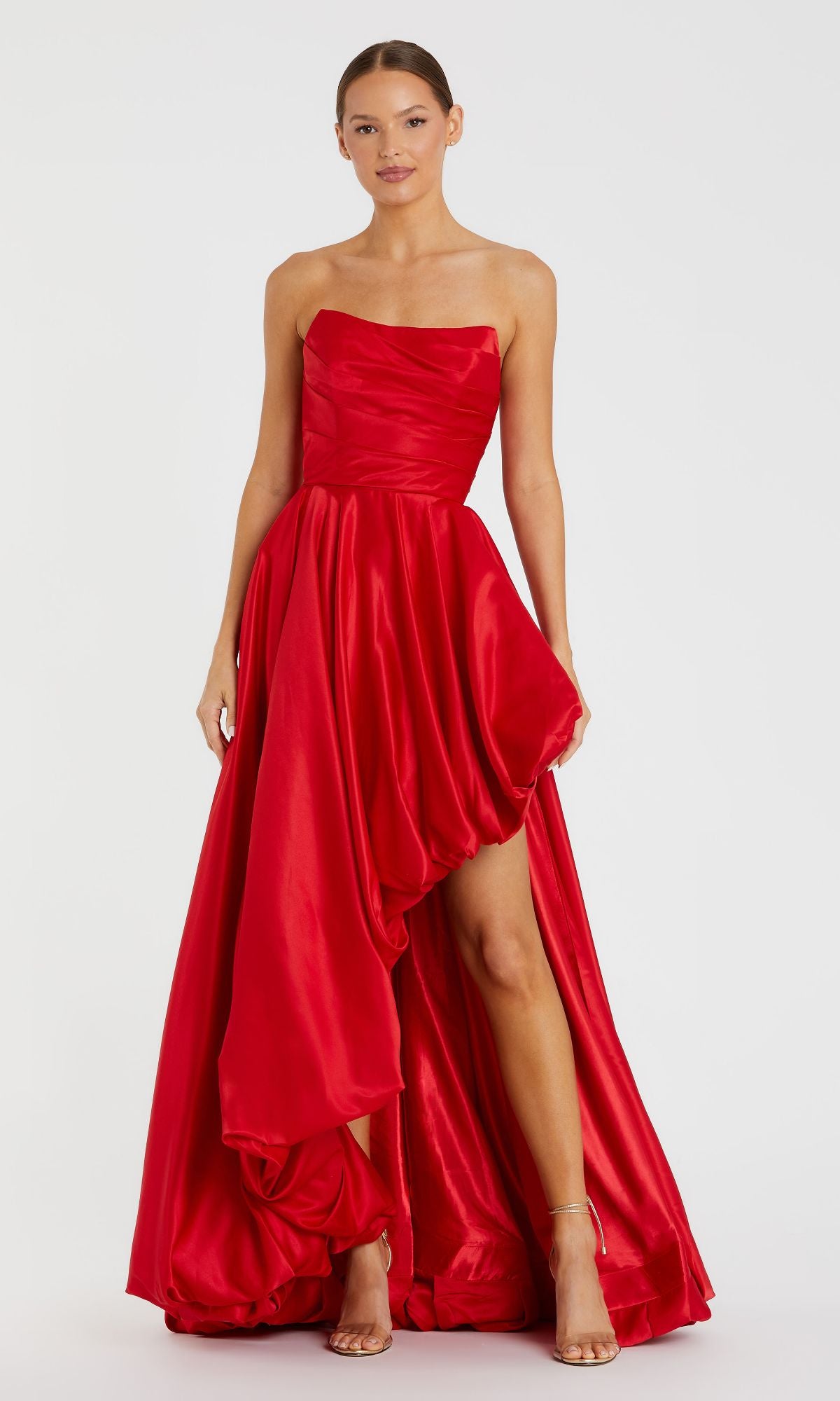 A woman stands against a white background wearing the Strapless Balloon Prom Dress: Mac Duggal 11685 in bright red, featuring a strapless neckline, ruched details, and an asymmetrical high-low hem.