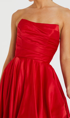 A person wearing the Strapless Balloon Prom Dress: Mac Duggal 11685, a bright red satin high-low gown with a fitted ruched bodice and a flared skirt.