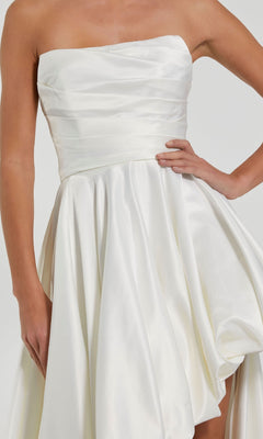 A woman in a strapless white satin Mac Duggal 11685 balloon prom dress with a fitted bodice and flared skirt stands with one hand on her hip.