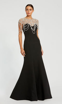 A woman in the Mac Duggal 11775 Pearl-Neckline Long Formal Dress—a fitted, floor-length black gown with a sheer beaded capelet adorned with draped pearl strands.
