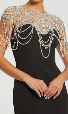 A woman wearing the Mac Duggal 11775 Pearl-Neckline Long Formal Dress, featuring a fitted black silhouette adorned with an ornate overlay of pearls and crystals across the shoulders and chest.