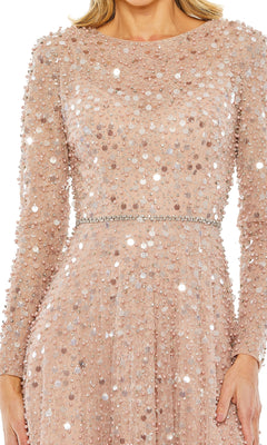 A person wearing the Mac Duggal 11782 Long Sleeve Sequin Formal Gown in blush, featuring sequins and a thin jeweled belt at the waist.