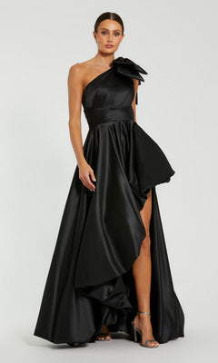 A woman models the Mac Duggal 11800 Bow Long Bubble Prom Dress in black, featuring a one-shoulder design with a large shoulder ruffle and high slit, against a plain background.