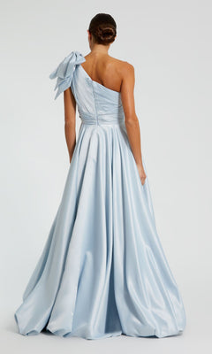 Woman wearing the Mac Duggal 11800 Bow Long Bubble Prom Dress, a light blue one-shoulder A-line evening gown with a large bow on the shoulder, stands with her back to the camera.