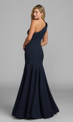 A woman poses against a plain gray background, looking over her shoulder at the camera while wearing the fitted, floor-length Beaded-One-Shoulder Prom Gown by Mac Duggal (style 11810) in navy.