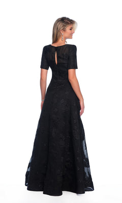 A woman is shown from the back against a white background, wearing the Dave and Johnny 11815 modest black prom dress—floor-length with short sleeves and a subtle textured pattern.