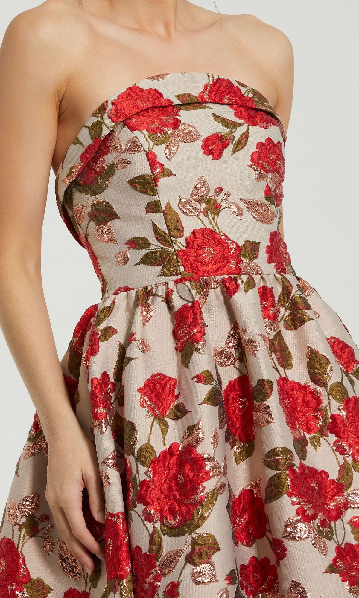 A woman models the Mac Duggal 11827 Strapless Print Formal Dress, featuring a beige base and red floral pattern, shown from shoulders to above the knees.