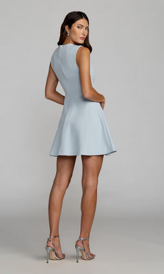 A woman stands against a plain background, looking over her shoulder in the Short A-Line Cocktail Dress: Mac Duggal 11829 (light blue), paired with silver high-heeled sandals.