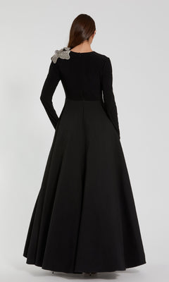A person is seen from the back wearing the Mac Duggal 11832 long sleeve black formal dress, an elegant A-line gown that features a decorative bow on one shoulder.