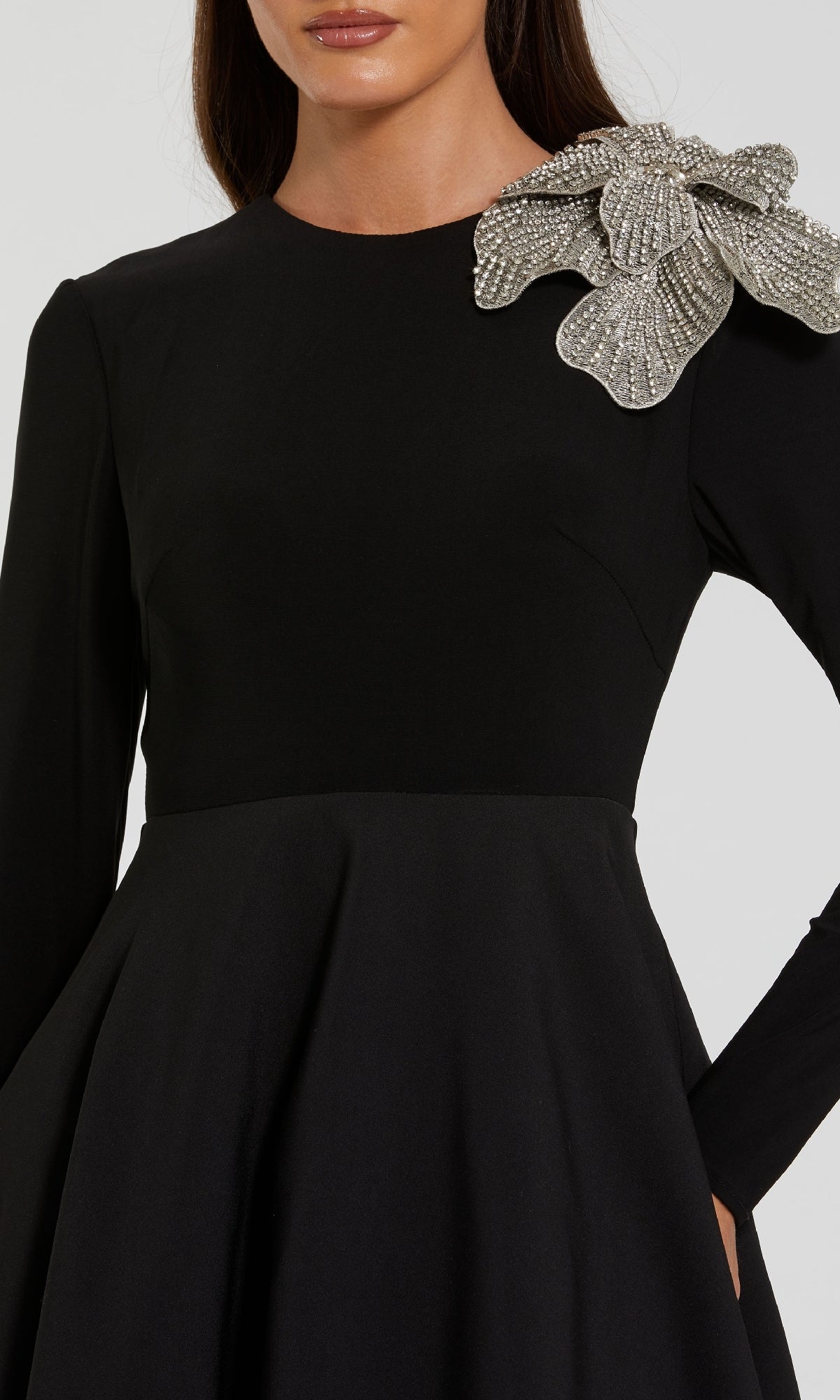 A woman wears the Mac Duggal 11832 Long Sleeve Black Formal Dress, styled with an A-line silhouette and adorned with a silver rhinestone flower on the shoulder.