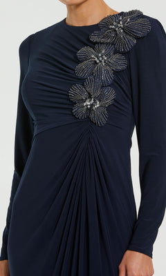 A woman wearing the Mac Duggal 11850, a dark blue long formal dress with beaded floral shoulder embellishments and gathered fabric detail—an elegant choice for a mother of the bride.