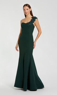 Woman wearing a dark green one-shoulder evening gown with floral details on a white background