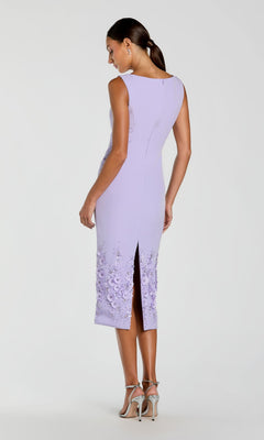 A woman models the Mac Duggal 11853 midi sheath wedding guest dress in light purple, sleeveless, featuring beaded 3-D flowers near the hem and a back slit, paired with silver high-heeled sandals.